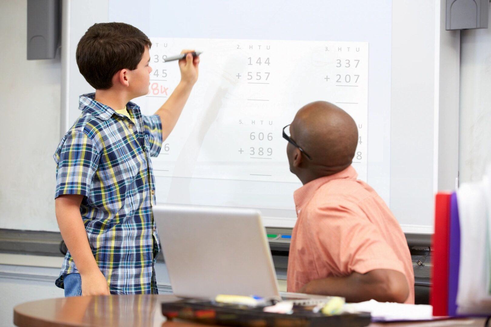 A boy is writing on the board while another man watches.