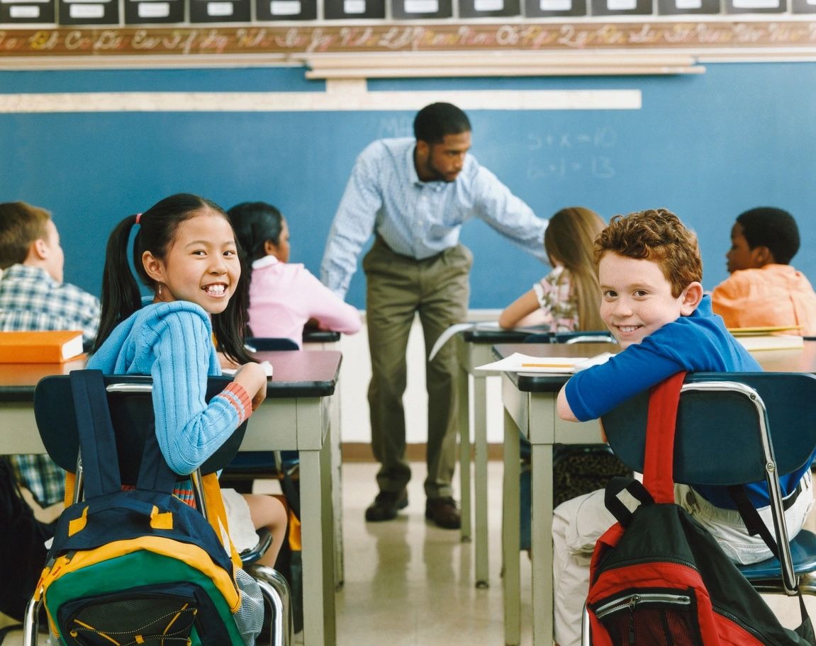 A group of children sitting at desks in front of a teacher.