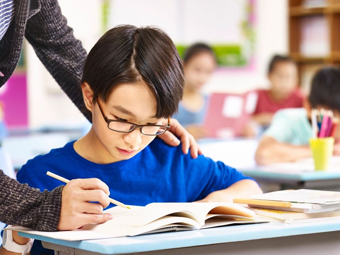 A boy is writing in his notebook while reading.