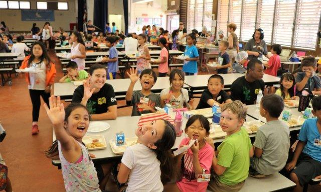 A group of children sitting at tables eating food.