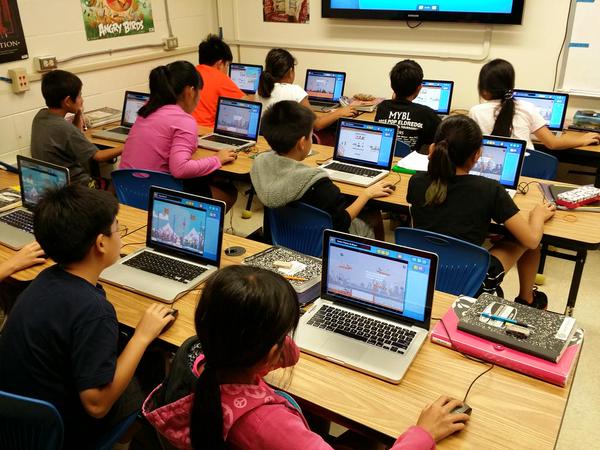 A group of children sitting at desks with laptops.