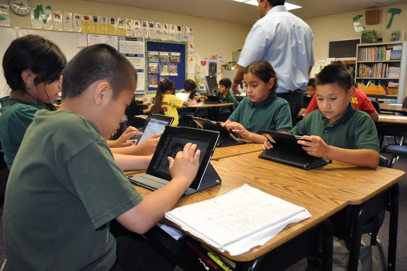 A group of kids sitting at a table with laptops.